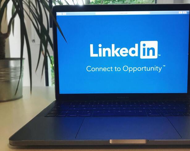 A close up of a computer on a desk. The computer has a blue screen with the LinkedIn Logo and a saying that says "Connect to Opportunity"