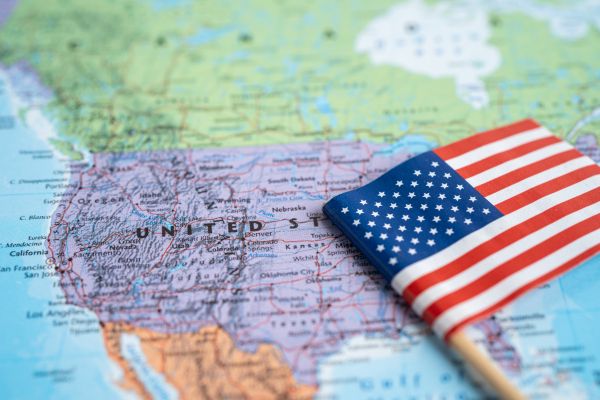 An image of the map specifically showing North America with the United States in the most focus. An American Flag is laying on top of the map.
