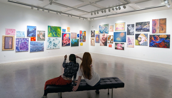 Two people looking at art work displayed in a gallery style. 