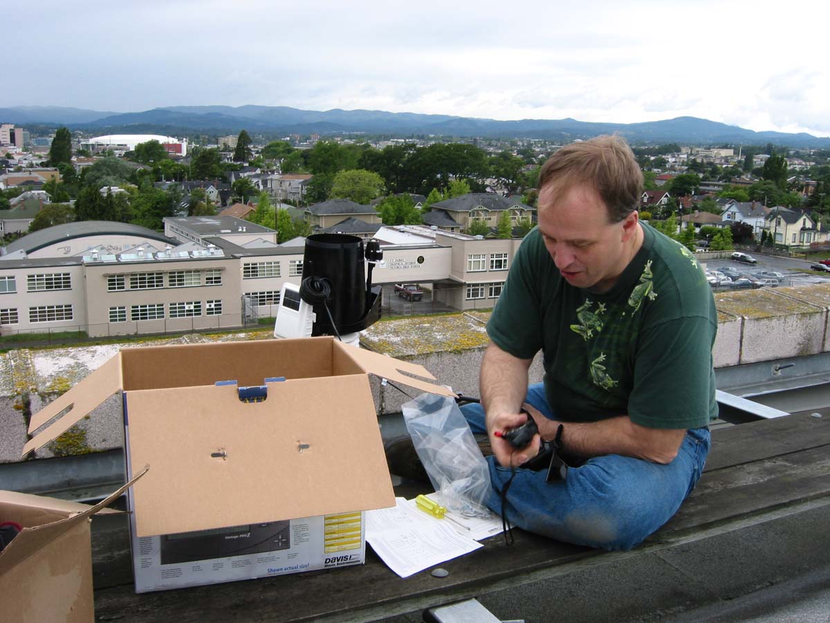 A man working with weather equipment on a roof overlooking a school